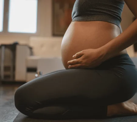 Femme enceinte étant assise sur ses genoux et touchant son ventre