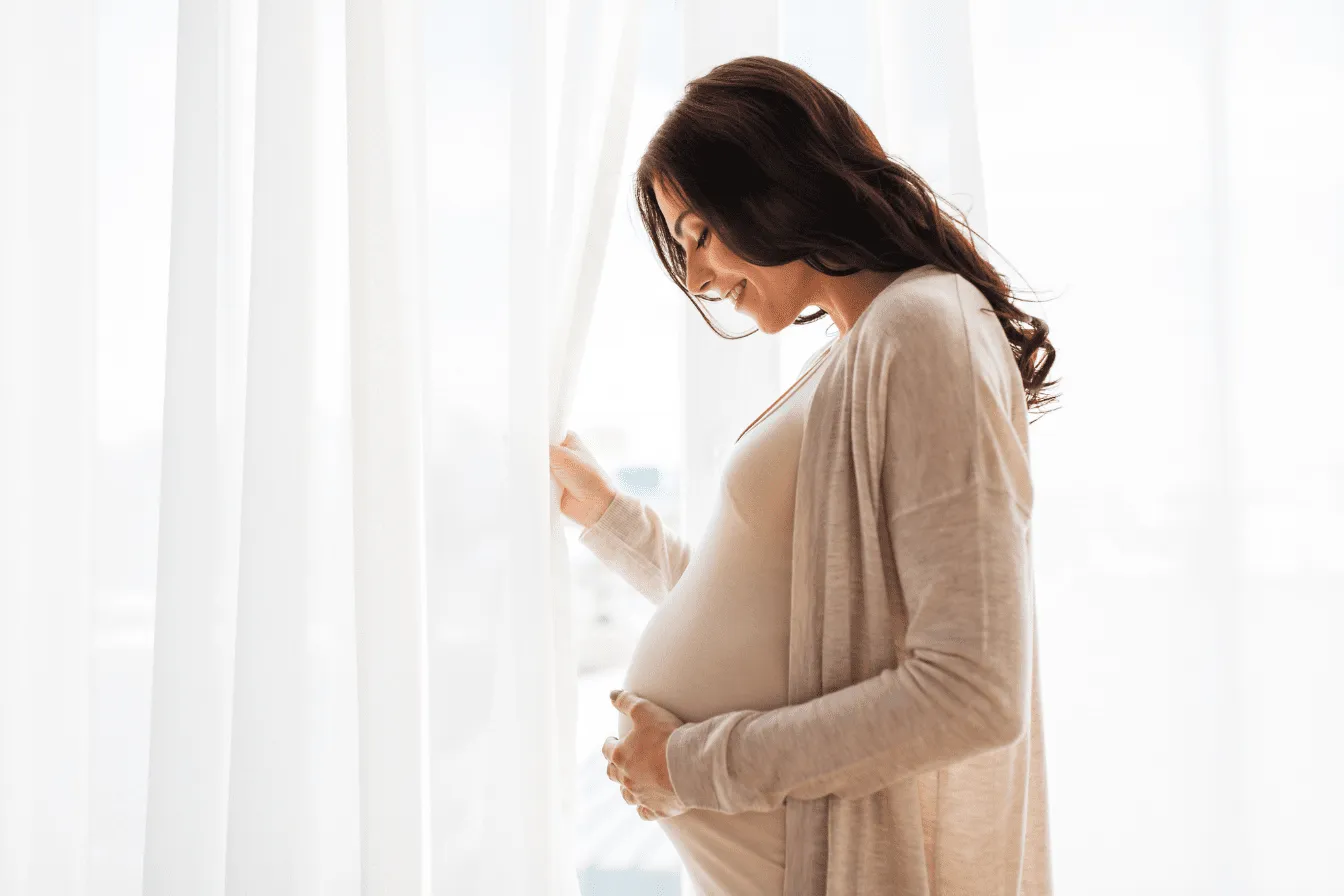 Femme enceinte proche d'une fenêtre touchant son ventre